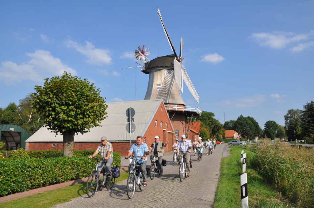 Große Fahrradgruppe fährt an der Mühle in Warsingsfehn vorbei